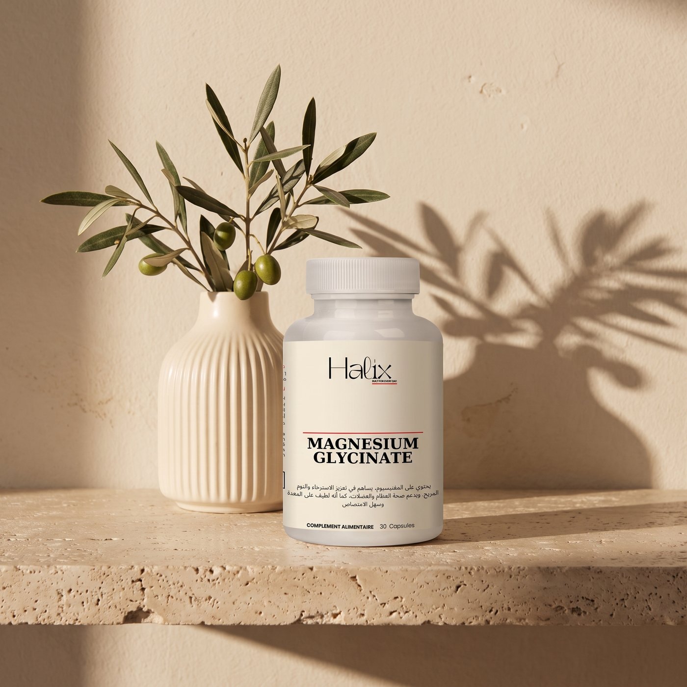 Flacon Halix Magnesium Glycinate posé sur une pierre, branche d’olivier